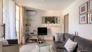 A modern living room with a grey sofa, a glass coffee table, a flat-screen TV, and a decorative mirror.