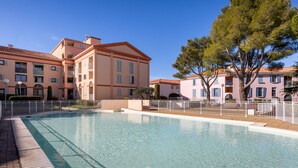 A swimming pool surrounded by a white fence, with buildings in the background.