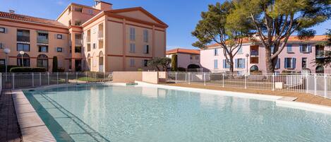 A swimming pool surrounded by a white fence, with buildings in the background.