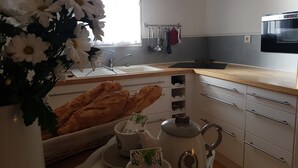 Une cuisine équipée d’un évier, d’un four à micro-ondes, d’une fenêtre avec des rideaux et d’un bouquet de fleurs.
