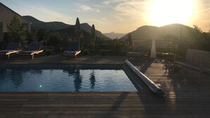 Una terraza de madera con piscina, sillas de descanso y un banco.