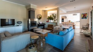 Una sala moderna con sofá, televisor, piano y un comedor al fondo.