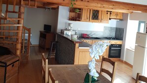 A spacious kitchen with wooden cabinets, a dining area with a wooden table and chairs, and a staircase leading to an upper level. - Converted barn in a small village 5 minutes from langeac (Langeac)