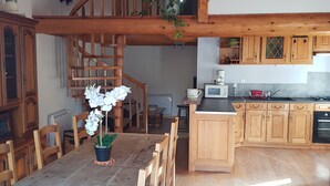 A spacious kitchen with wooden cabinets, a dining area with a wooden table and chairs, and a staircase leading to an upper level. - Converted barn in a small village 5 minutes from langeac (Langeac)