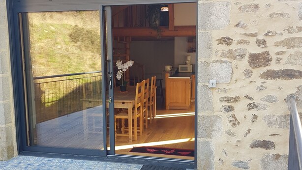 A stone building with a sliding glass door leading to an interior with wooden furniture and a small kitchen area. - Converted barn in a small village 5 minutes from langeac (Langeac)