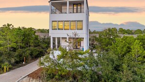 A two-story building with a balcony, surrounded by dense greenery and a clear sky. - Aces High|Private Beach Access|Private Pool|Golf Cart (Santa Rosa Beach)