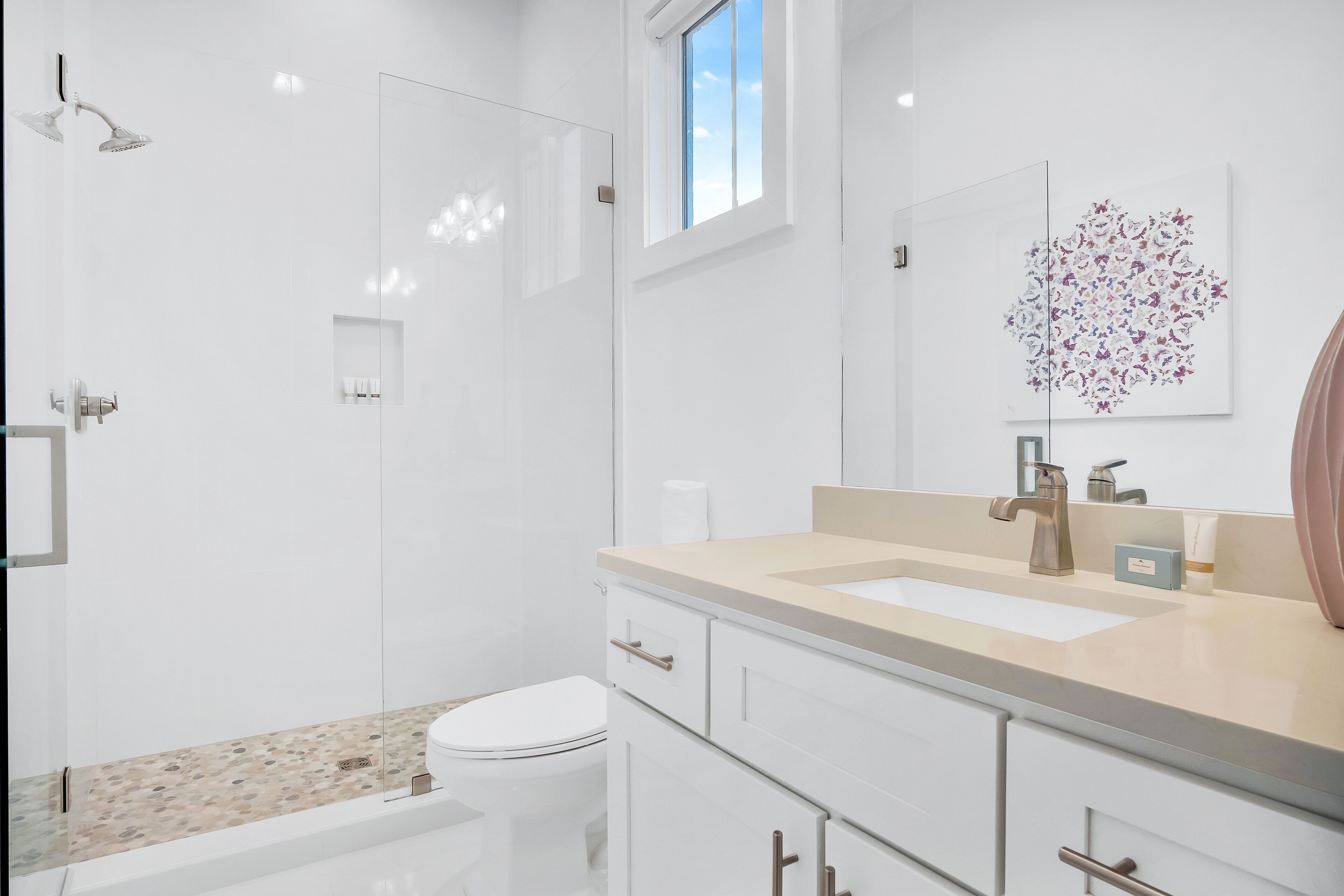 Une salle de bain moderne avec une douche à parois de verre, des toilettes, un lavabo doté d’un plan de toilette beige et un grand miroir.