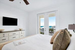 Ein Schlafzimmer mit Bett, Kommode, Flachbildfernseher und einem Balkon mit Meerblick.