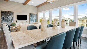 A spacious room with a large wooden dining table, blue upholstered chairs, a flat-screen TV mounted on the wall, and large windows offering a view of the neighborhood. - Aces High|Private Beach Access|Private Pool|Golf Cart (Santa Rosa Beach)