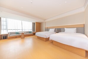 Habitación de hotel con dos camas, un sofá, una mesita y una ventana con cortinas.