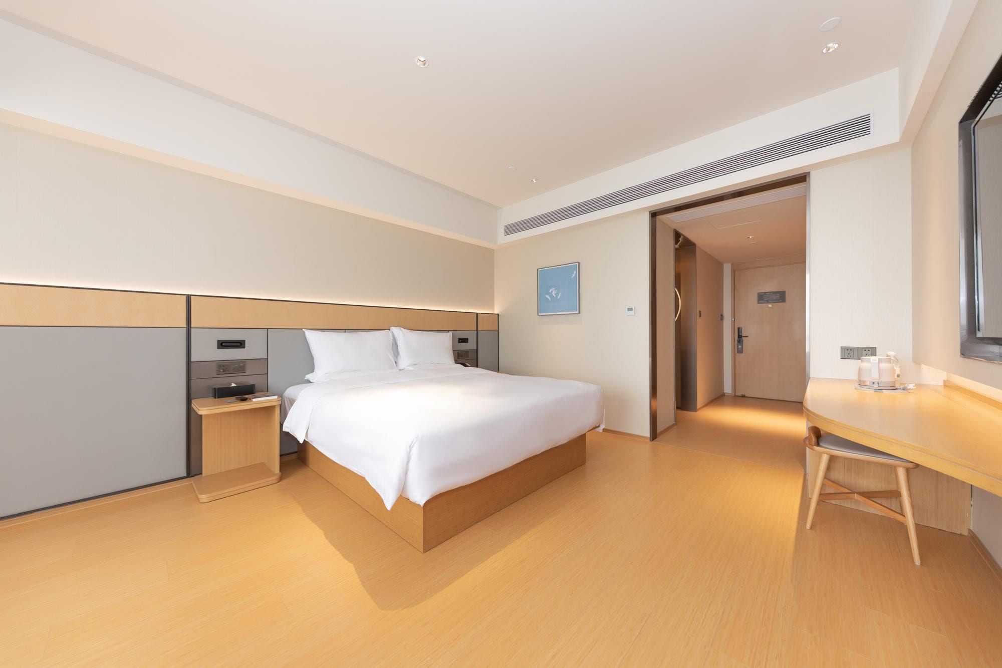 Ein modernes Hotelzimmer mit einem großen Bett, Nachttischen, einem Schreibtisch und einer Tür zu einem weiteren Raum.