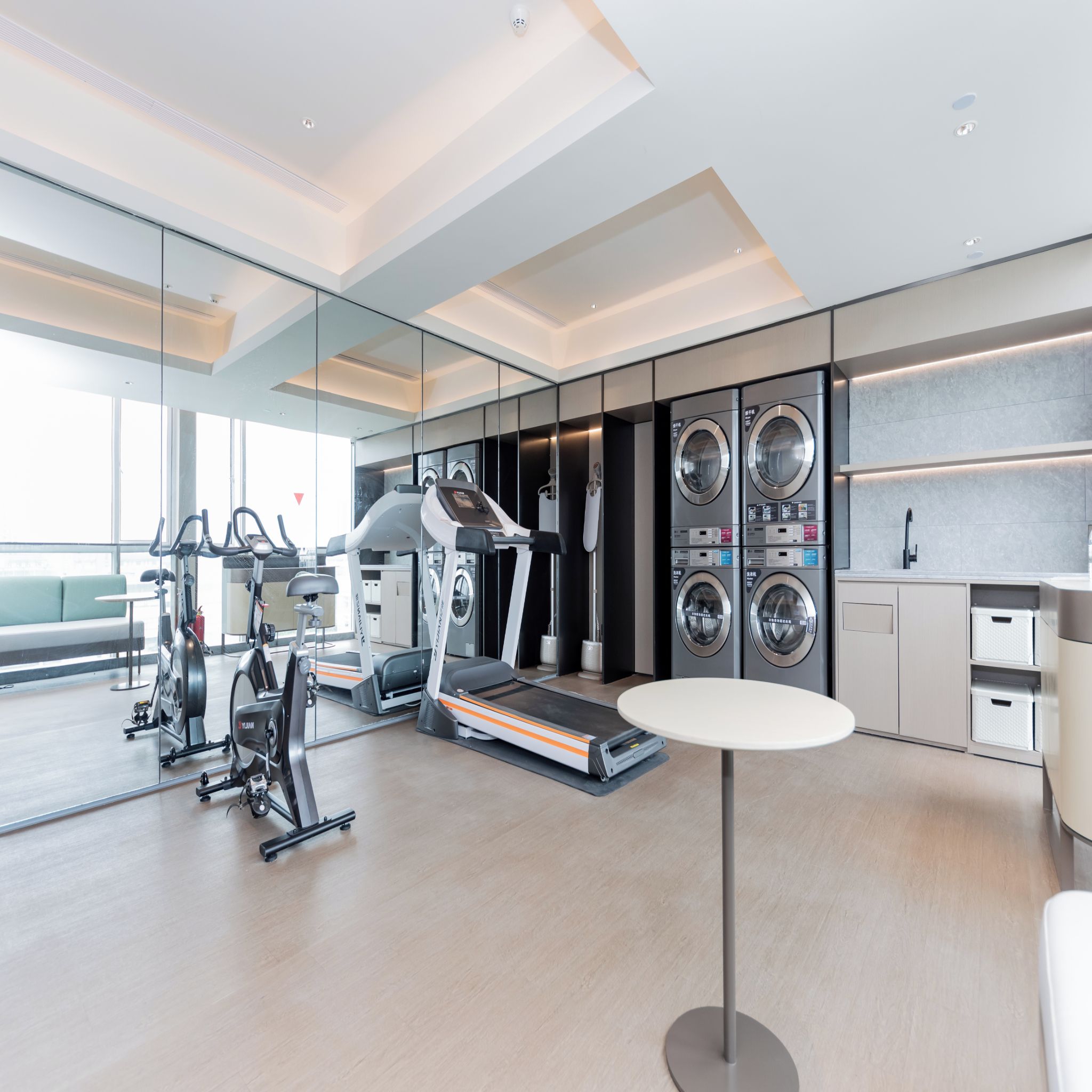 A modern gym with cardio machines, a treadmill, and a wall-mounted washing machine.