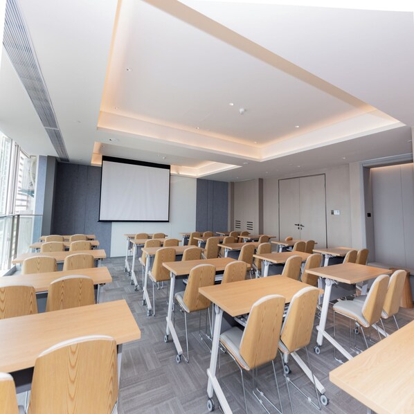 A modern conference room with rows of desks and chairs, a large screen, and a door with a lock. - Ji Hotel (Suzhou)