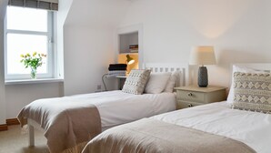 A bedroom with two beds, a bedside table with a lamp, a window with a view of flowers, and a ceiling light. - 3 bedroom accommodation in Johnshaven, near Stonehaven (Johnshaven, near Stonehaven)