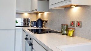 A modern kitchen with white cabinets, a built-in oven, a coffee maker, and a kettle on the countertop. - 3 bedroom accommodation in Johnshaven, near Stonehaven (Johnshaven, near Stonehaven)
