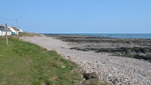 A coastal area with a rocky beach, a grassy area, and a building with a white facade and a blue roof. - 3 bedroom accommodation in Johnshaven, near Stonehaven (Johnshaven, near Stonehaven)