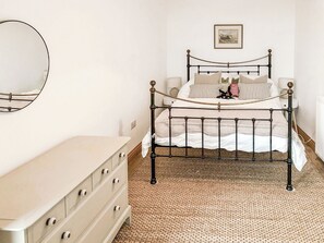 Quarto com cama de estrutura metálica, cômoda, espelho e quadro na parede.