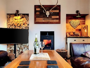 A cozy living room with a fireplace, a television, and a dining table set with wine glasses and a bottle.