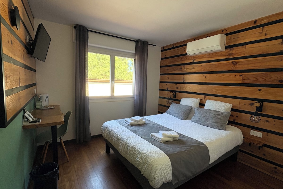 A bedroom with a bed, a desk, and a window.