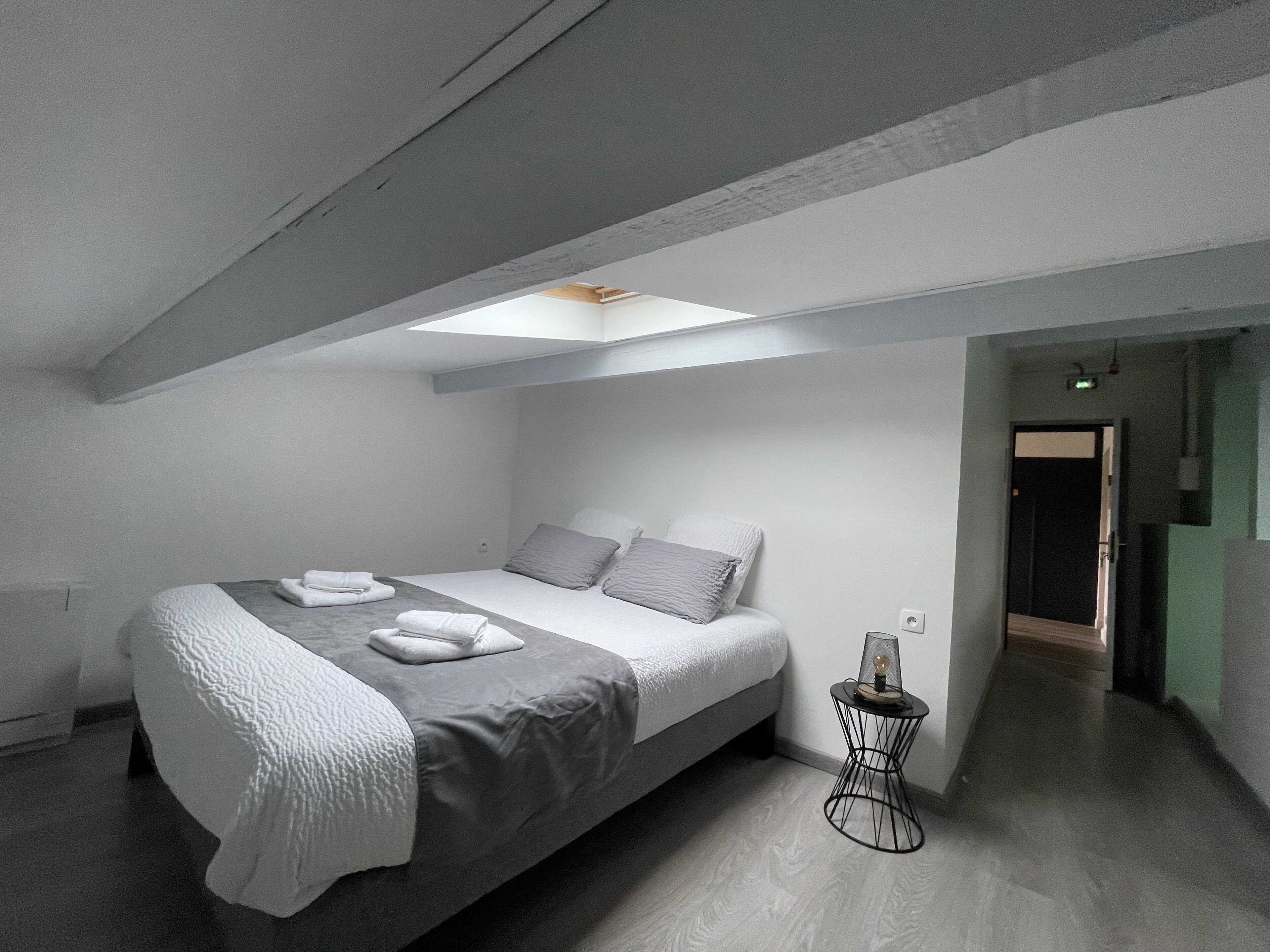 Camera da letto moderna e minimalista con finestra a lucernario, un letto rifatto e un tavolino laterale.