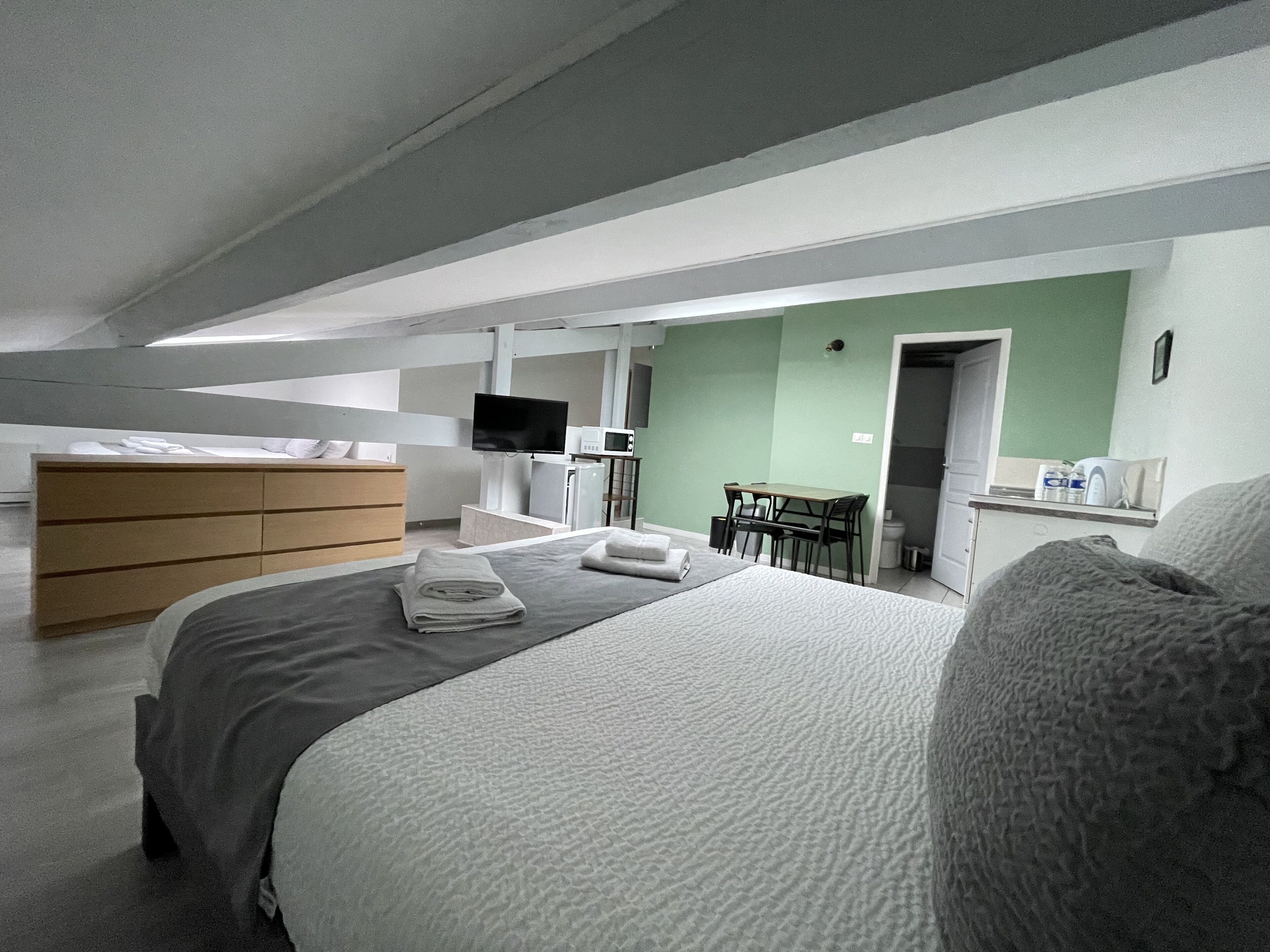 Habitación de hotel moderna con una cama, un aparador de madera, un escritorio con una silla, un televisor y un microondas.