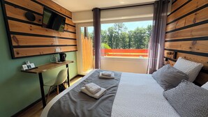 Habitación de hotel con cama, escritorio, silla, televisión montada en la pared y balcón con vista a árboles y una valla roja.