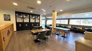 Un restaurante con mesas y sillas de madera, una partición negra con paneles decorativos y vistas a zonas verdes a través de amplios ventanales.