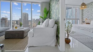 Een moderne slaapkamer met uitzicht over de stad, een witte bank, een bed met beddengoed met een patroon, en een groot raam.