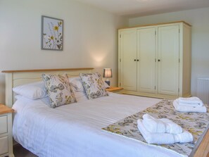 A bedroom with a bed, floral pillows, a nightstand, a lamp, and a wardrobe.