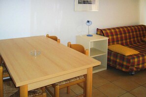 A room with a wooden table, chairs, a sofa with a plaid cover, and a small white cabinet. - Spacious Corsica Stay for 8 near Beach (Ghisonaccia)