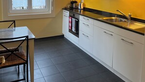 Une cuisine avec des meubles blancs, un plan de travail noir et une fenêtre à vitrage dépoli.