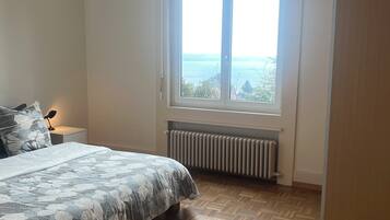 Ein Schlafzimmer mit einem Bett, einem Fenster mit Blick, einem Heizkörper und einer Pendelleuchte.