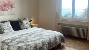 Une chambre à coucher comprenant un lit, une table de chevet, une lampe, un radiateur et une fenêtre donnant sur un beau paysage.