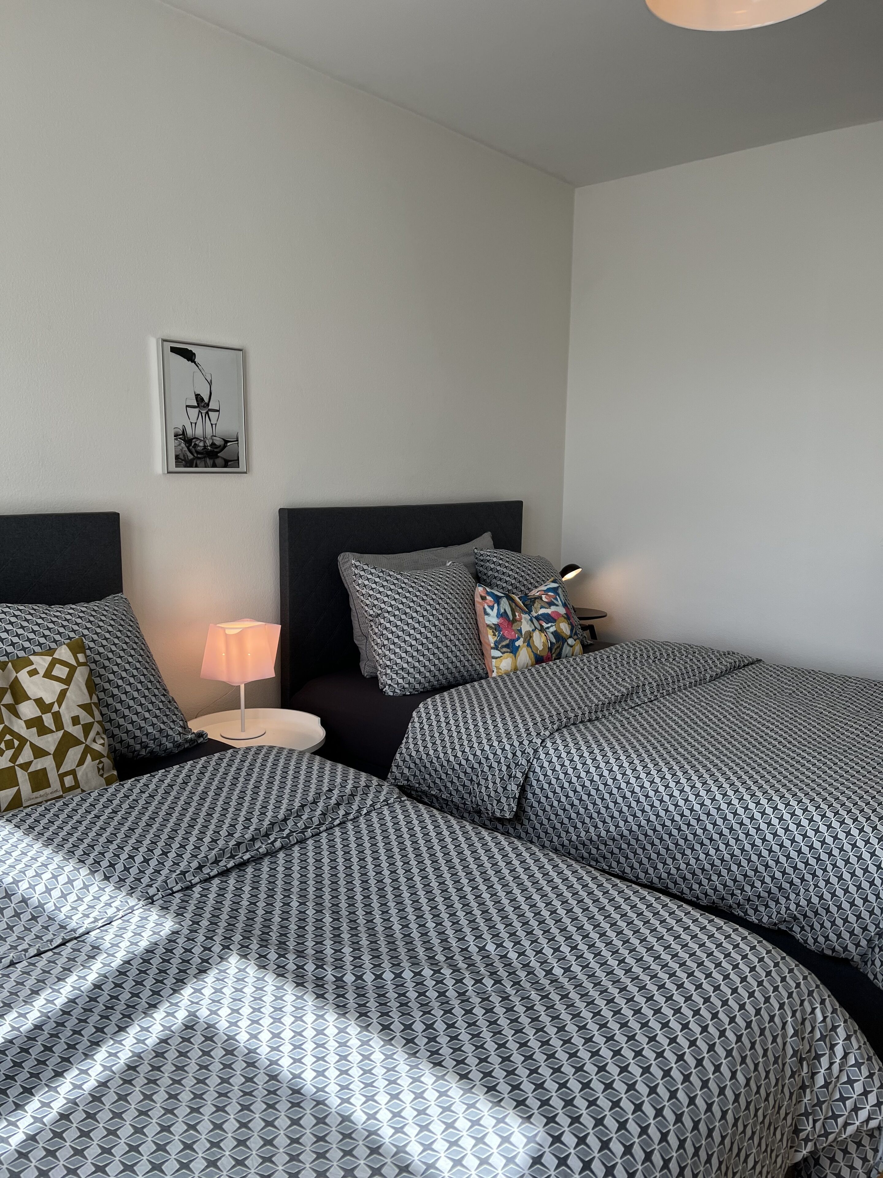 A hotel room with two beds, a nightstand, a lamp, and a framed picture on the wall.