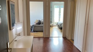 Un couloir au plancher de bois menant à une chambre à coucher équipée d’un lit et d’une fenêtre.