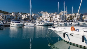 Un port esportiu amb nombroses embarcacions amarrades, envoltat d'edificis blancs amb balcons i palmeres.