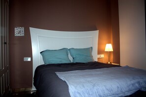 A neatly made bed with a white headboard and teal pillows in a room with brown walls and a bedside lamp.