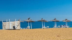 Una platja amb paraigües i gandules, un cotxet i un cel blau i clar.