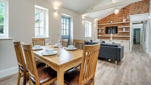 Un comedor con una mesa y sillas de madera, una puerta azul y una pared de ladrillo con estantes y un televisor.