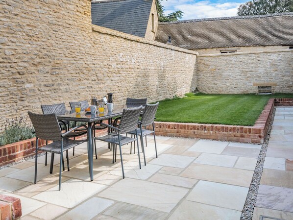 A stone wall, a grassy lawn, and a patio with a table and chairs.
