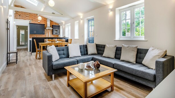 Una sala de estar moderna con sofá, mesa de centro y zona de comedor con pared de ladrillo y muebles de madera.
