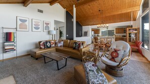 A spacious living room with a high ceiling, wooden beams, a brown leather sofa, a patterned armchair, and a dining area with wooden furniture. - Mountain Views at Rim Country Chalet  (Payson)