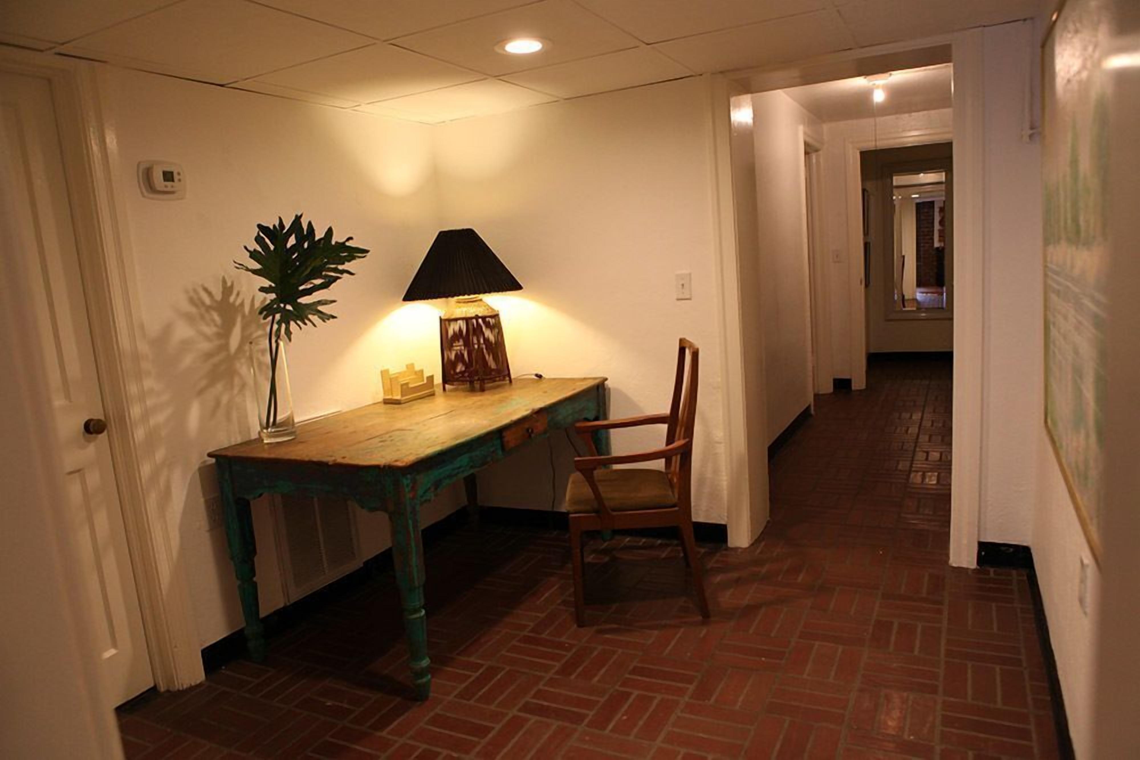 A hallway with a wooden desk, a chair, a lamp, and a potted plant.