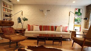A living room with a white brick wall, a cowhide rug, a sofa with colorful pillows, a leather chair, and a bull skull decoration. - Elegant Savannah Patio Apartment! An Arty Flair on Jones Street (Savannah)