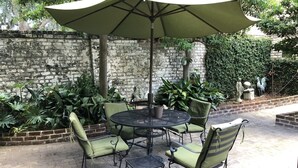 A patio with a round table and chairs, an umbrella, and a brick wall. - Elegant Savannah Patio Apartment! An Arty Flair on Jones Street (Savannah)
