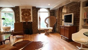 A living room with a brick wall, wooden flooring, a cowhide rug, a television, and a bookshelf. - Elegant Savannah Patio Apartment! An Arty Flair on Jones Street (Savannah)