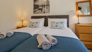 A hotel room with a bed, two pillows with bird designs, a bedside lamp, a wooden nightstand, a mirror, and a wall art piece. - The Old Mill (Keswick)