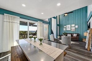 Un salon moderne avec une longue table à manger, un canapé et une vue sur l’extérieur.