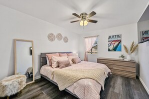 Une chambre à coucher comprenant un lit, une commode, un ventilateur de plafond et des œuvres d’art décoratives accrochées au mur.
