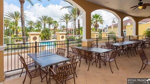 An outdoor patio area with tables and chairs, a pool in the background, and palm trees. - Paradise Villa in Regal Palms (Davenport)